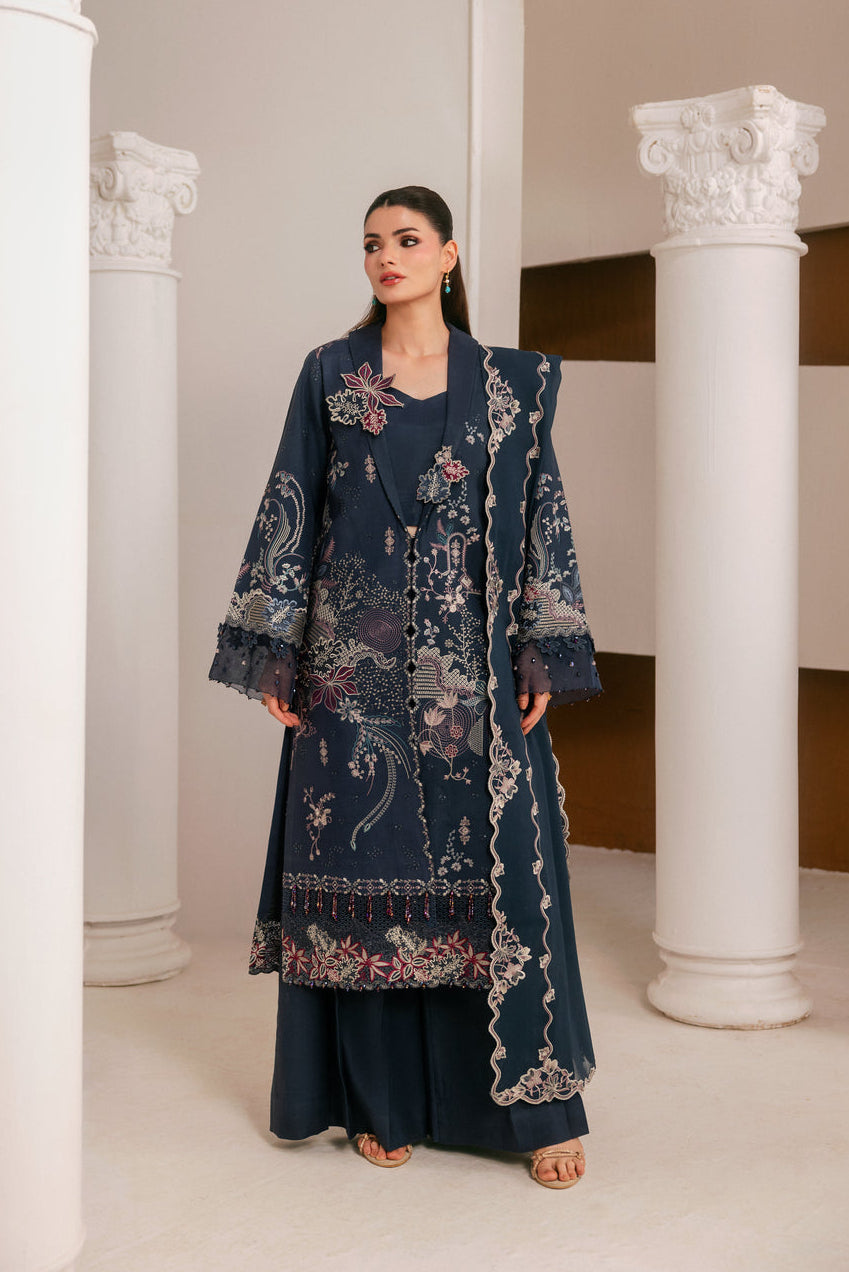 A woman modeling a dark navy blue embroidered traditional outfit with matching pants, standing between white classical columns in an indoor architectural setting.